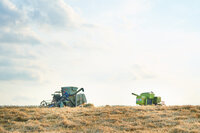 Foto: Zwei Mähdrescher stehen auf einem abgeernteten Feld unter einem bewölkten Himmel. Die Maschinen sind grün und blau und befinden sich links und rechts im Bild.