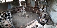 Foto: Eine verlassene industrielle Umgebung mit Metallstrukturen, Paletten und einer Leiter. Der Raum wirkt ungepflegt und enthält verschiedene Metallteile und Kabel.