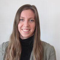 Foto: Eine Person trägt einen grauen Blazer und einen schwarzen Rollkragenpullover vor einem neutralen Hintergrund.