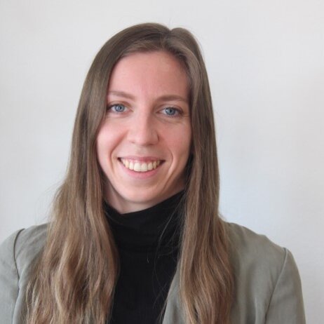 Foto: Eine Person trägt einen grauen Blazer und einen schwarzen Rollkragenpullover vor einem neutralen Hintergrund.