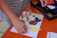 Foto: Eine Person arrangiert Korken, Papier und andere Materialien auf einem Tisch für ein Bastelprojekt. Verschiedene Bastelmaterialien sind in einem Organizer sichtbar.